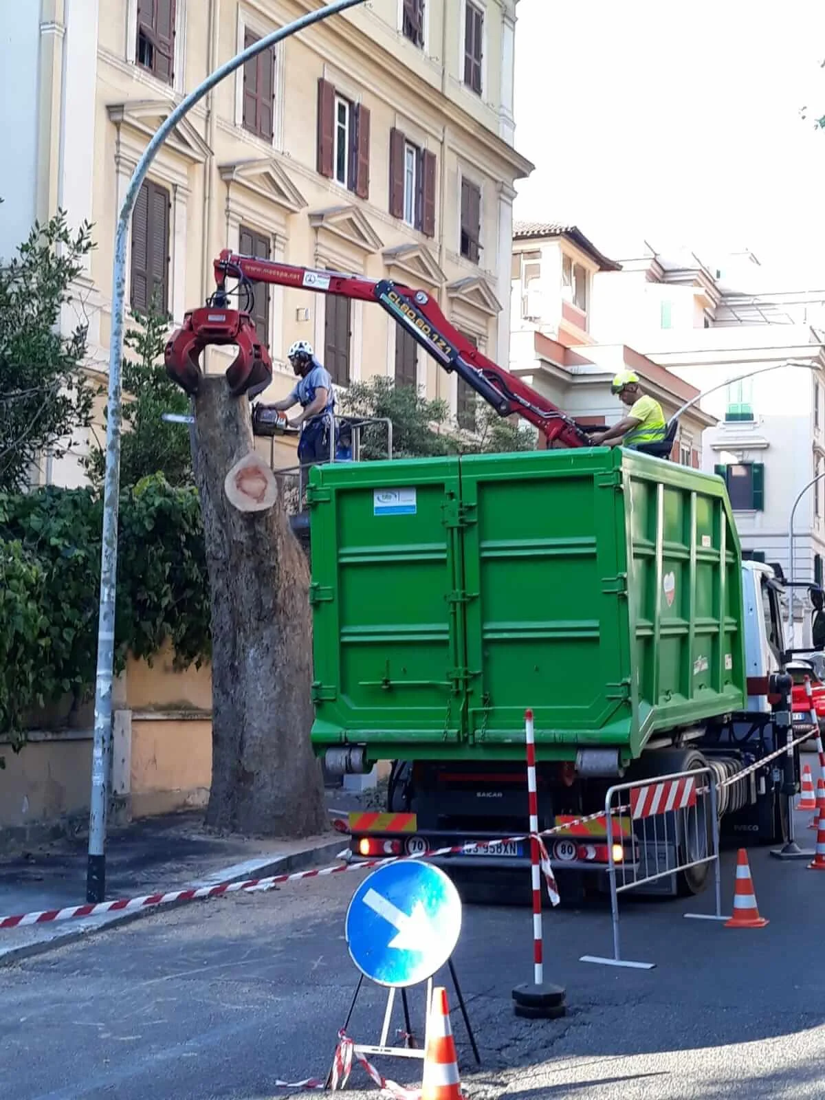Rimozione di sezioni di tronco con gru in una strada di Roma, area cantiere segnalata